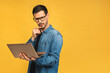 Concentrated on work. Confident young handsome man in casual working on laptop while standing against yellow background.