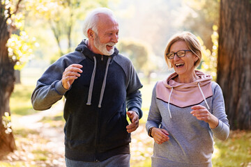 Wall Mural - Smiling senior couple jogging in the park. Sports activities for elderly people.