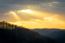 Yellow Sun Rays Shining Through Dark Clouds Over Forest Silhouette