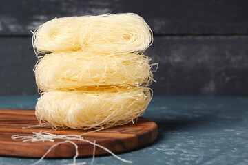 Wooden board with raw rice noodles on dark table