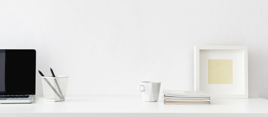 Wall Mural - Desk with white office supplies, mug, frame, laptop and empty space. Mockup.