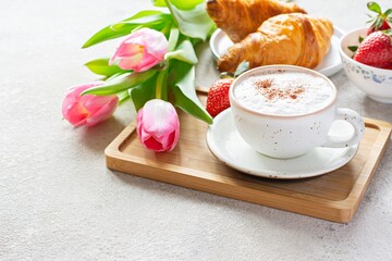 Happy mother's day, beautiful breakfast, lunch with cup of coffee (cappuccino) fresh croissants, strawberries on tray, bouquet of tulips as gift. Festive concept. Spring holiday, family relations.