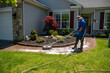 Handyman using a circular power washer to clean a brick walkway in front of a house