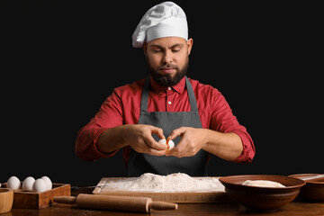 Canvas Print - Male baker breaking egg for dough at table on dark background