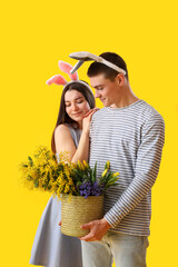 Wall Mural - Happy young couple in bunny ears with flowers on yellow background. Easter celebration