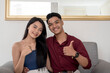 © Mdv Edwards - A young asian couple giving their seal of approval while sitting at the couch of their apartment. Two people making a thumbs up sign.