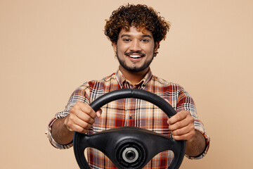 Smiling cheerful fun cool young Indian man wearing brown shirt casual clothes hold steering wheel driving car isolated on plain pastel light beige background studio portrait. People lifestyle concept.