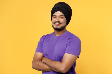 Wall Mural - Happy devotee Sikh Indian man ties his traditional turban dastar wear purple t-shirt hold hands crossed folded look camera isolated on plain yellow background studio portrait People lifestyle concept