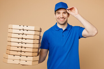 Smiling happy delivery guy employee man wear blue t-shirt uniform workwear work as dealer courier hold pizza in cardboard flatbox touch cap isolated on plain light beige background. Service concept.