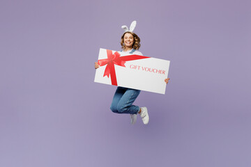 Wall Mural - Full body young woman wear casual clothes bunny rabbit ears hold store big gift certificate coupon voucher card isolated on plain pastel light purple background studio. Lifestyle Happy Easter concept.