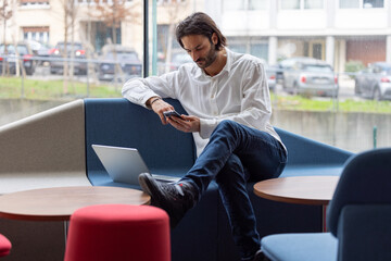 Poster - portrait d'un jeune homme d'affaires ou employé de bureau qui travaille sur son ordinateur portable dans un bureau confortable et qui communique avec son téléphone portable