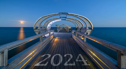 2024 written on the wooden planks of a pier. Happy new year 2024 relaxation on the seashoreafter sunset. 2024 concept with illuminated pier on the Baltic Sea resort of Kellenhusen after sunset.