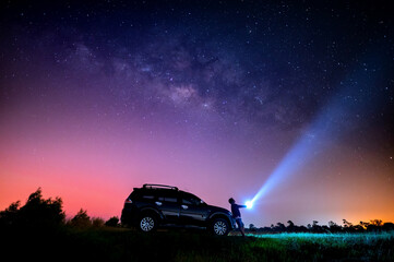 Wall Mural - man tourist with flashlight near his camp car at night. space background with noise and grain. night