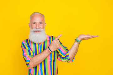 Poster - Photo of positive retired man with white beard dressed striped shirt demonstrate directing empty space isolated on yellow color background