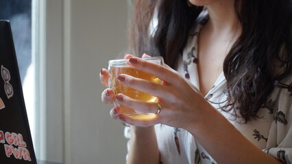 A woman holds a cup of green tea in front of a laptop.