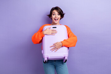 Sticker - Photo of cheerful exited glad lovely lady wear orange stylish clothes hold suitcase fly abroad isolated on purple color background