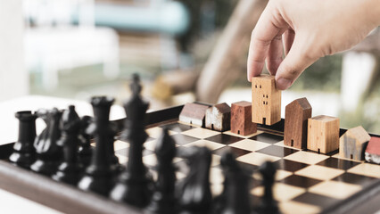 Hand of business man moving chess to Building and house models in chess game, competition success play. strategy, management or leadership concept