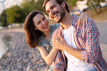 Wall Mural - Happy young couple in love. Pretty girl cuddling with boyfriend on beach and bright warm lens flare.
