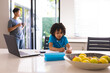 © Wavebreak Media - Hispanic boy writing while doing homework at dining table with father in background
