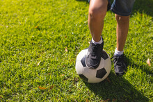 High Angle Low Section Of Hispanic Boy Stepping On Soccer Ball At Backyard On Sunny Day
