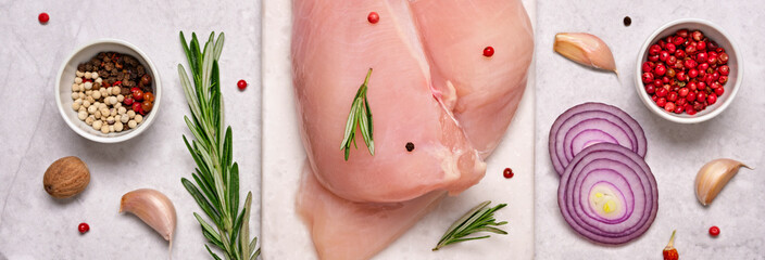 Fresh chicken breast fillet on cutting board with spices and herbs on gray marble background. Preparation for cooking, banner format