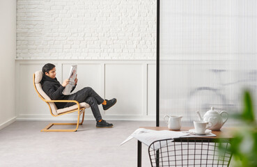 Rocker chair in the white room, man is reading newspaper, brick and classic wall background, chamber, green plant leaf close up blur, working table.