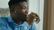 © Yuliia - African american healthy man drinking water glass of cold fresh drink sit at home office feel thirsty hydrate body health care habbit keep aqua balance dreaming ethnic businessman looking at window