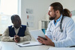 © pressmaster - Young doctor with tablet looking at African American senior male patient and listening to him during medical consultation in clinics