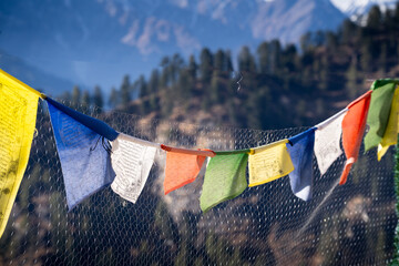 sacred religious multicolored prayer flags on fence moving in the wind showing a bhuddist prayer incantation common in hill stations in Himachal Pradesh