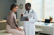 © pressmaster - Confident clinician with medical document communicating with happy mature female patient sitting on couchette in front of him