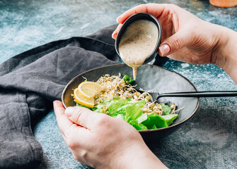 Girl holding bowl with mixed salad of lettuce, sprouted grains and microgreens with sesame sauce