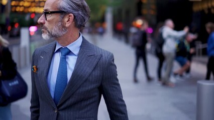 Wall Mural - Successful businessman in suit  with cellphone crosses city road t in financial district. Confident entrepreneur in stylish eye glasses walking forward outdoors in downtown. Slow motion 