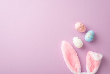 easter concept. top view photo of fluffy bunny ears and colorful easter eggs on isolated lilac backg