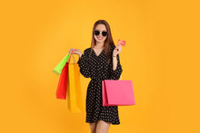 Happy Young Woman With Shopping Bags And Credit Card On Yellow Background. Big Sale