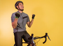 Medium Close Up Of The Excited Asian Man Sitting On The Bicycle With Clenched Arms On Isolated Background