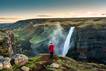 Wall Mural - Haifoss waterfall flowing in volcanic canyon and traveler taking a picture among the Icelandic Highlands in summer