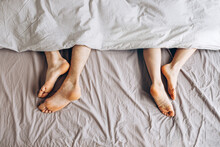 Sleeping Couple. Male And Female Bare Feet Under Duvet Lying On Bed Separately, Top View
