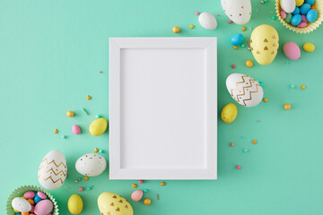 Wall Mural - Easter decoration concept. Flat lay photo of white photo frame colorful easter eggs and sprinkles on turquoise background with blank space