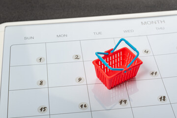 Small shopping cart on calendar background. Scheduled time for grocery shopping. Monthly grocery purchases