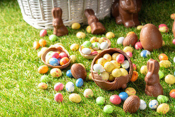 Wall Mural - Easter egg hunting background. Various candy and chocolate Easter eggs, bunny and rabbits with basket for eggs on green grass park or garden background