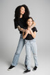 © LIGHTFIELD STUDIOS - Trendy mother hugging kid in jeans and t-shirt on grey background.