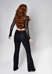 Sticker - Full length portrait of beautiful woman with long red hair wearing black corset top and leather pants. Standing pose, facing backwards walking away from camera. Isolated on white studio background.