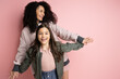 © LIGHTFIELD STUDIOS - Positive curly woman holding hand of preteen daughter on pink background.