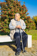 Portrait of ordinary Ukrainian senior man sitting on  bench against rowan tree and resting at sunny autumnal day