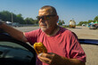 Portrait of hungry Ukrainian senior driver taking patty near his car while standing near Vasylivka, Zaporizhzhia Oblast, Ukraine