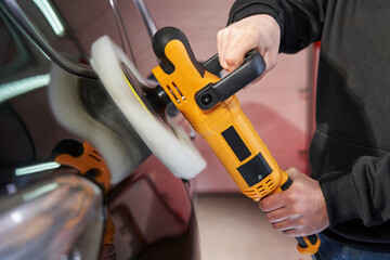 side view of a working yellow angle grinder with a polishing wheel. worker's hands