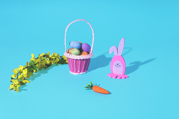 Wall Mural - Easter Bunny, eggs in basket, carrot and spring tree branch on cyan background. Minimal horizontal composition, Easter decoration concept