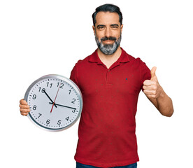 Sticker - Middle aged man with beard holding big clock smiling happy and positive, thumb up doing excellent and approval sign