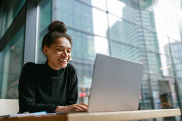 Smiling female freelancer working on laptop while sitting in cafe near window. Distance work 