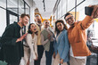© BullRun - Cheerful multiethnic colleagues taking selfie in office